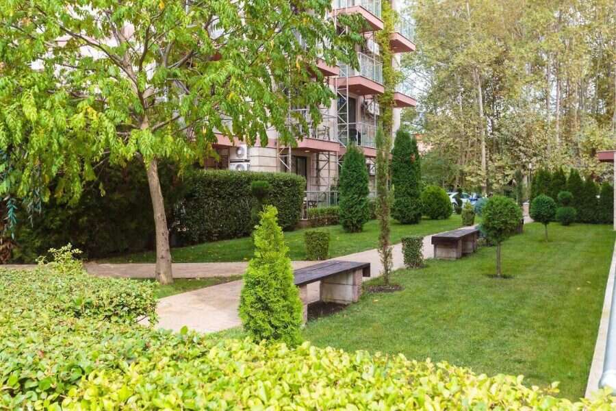 Modern apartment building with landscaped garden in Sunny Beach. Bright, sunny garden with benches, trees, and shrubs near Tarsis - Club & Spa.