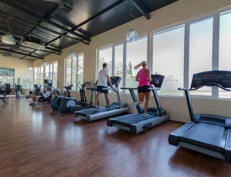 Gym with large windows and people running on treadmills for fitness.