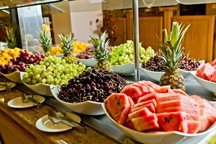 Fresh tropical fruits display at a buffet table in a bright, inviting setting. Vibrant assortment of grapes, pineapples, and watermelons at a sunny beach resort.