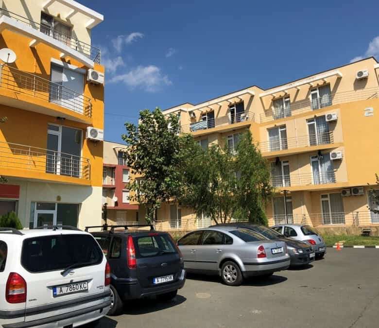 Bright yellow apartment complex with multiple balconies and parking area.