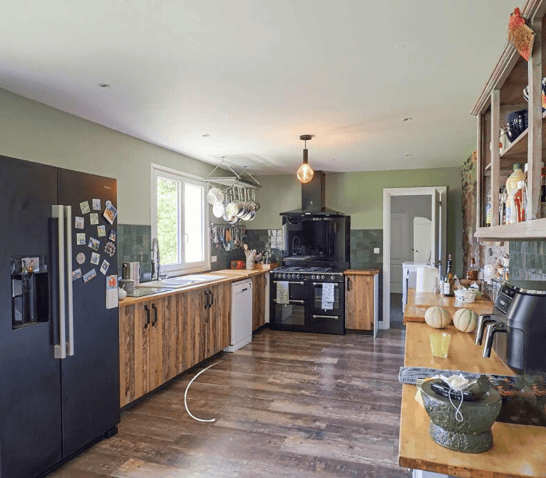 Spacious kitchen in Brittany gite with wooden cabinets, black appliances, and natural light. Perfect.