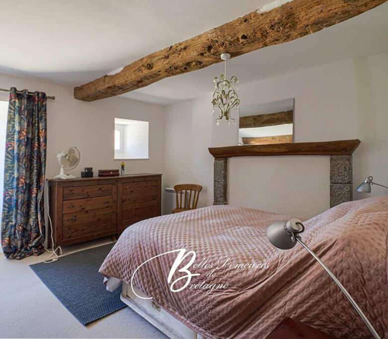 Cozy bedroom featuring rustic wooden beams and modern decor in the Gites du Manoir complex, ideal fo.