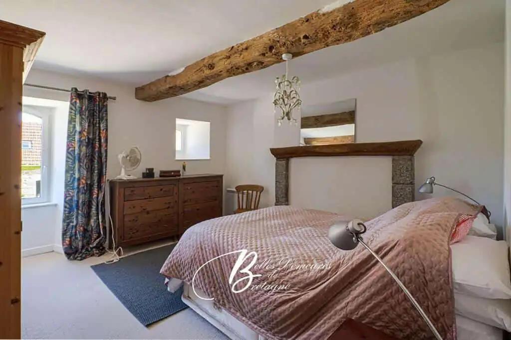 Cozy bedroom featuring rustic wooden beams and modern decor in the Gites du Manoir complex, ideal fo.