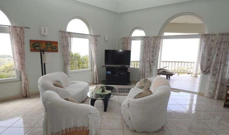 Spacious living room in a luxury villa featuring large windows and ocean views in Harmony Hall, Pros.