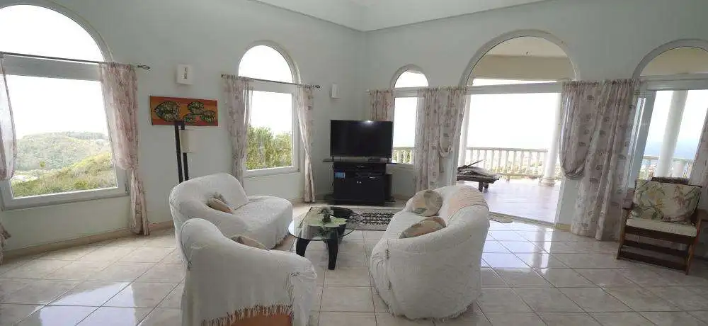 Spacious living room in a luxury villa featuring large windows and ocean views in Harmony Hall, Pros.
