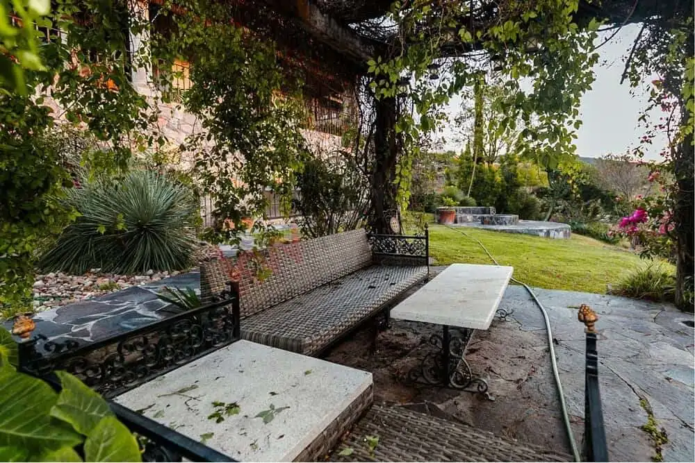 Elegant garden seating area with lush greenery and shaded trees. Outdoor seating with garden views and shaded trees in a peaceful estate setting.