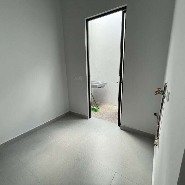Bright empty room with door to outdoor space and utility connections.