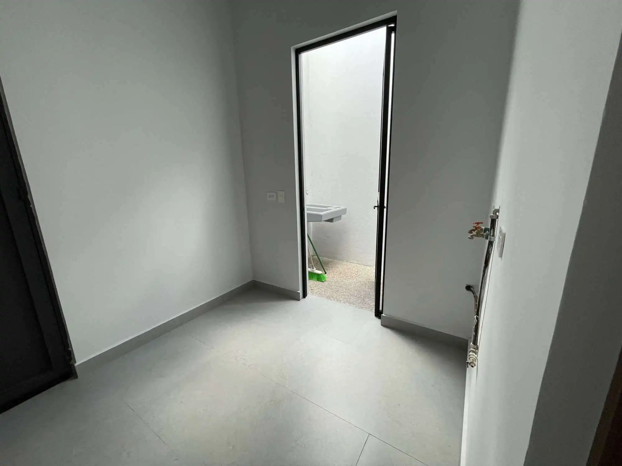 Bright empty room with door to outdoor space and utility connections.
