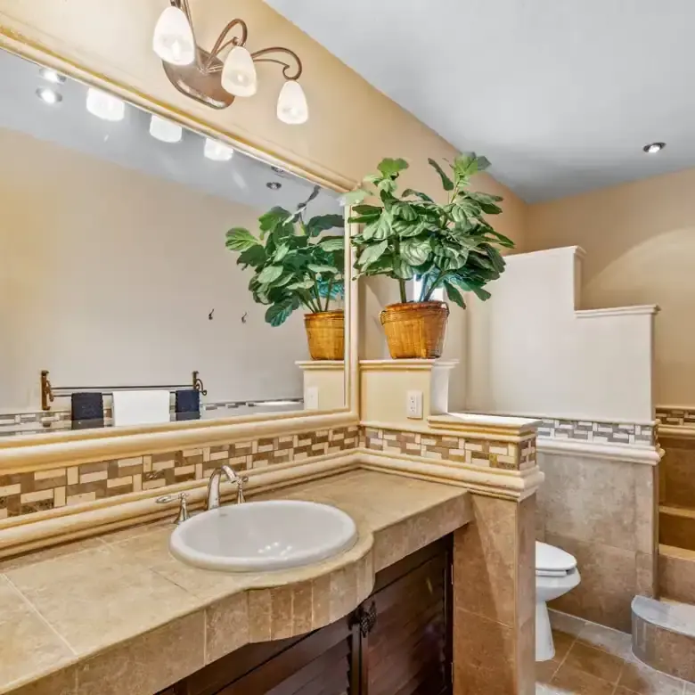 Bathroom with beige tiles, large mirror, and decorative plant accents in Rancho Los Labradores.
