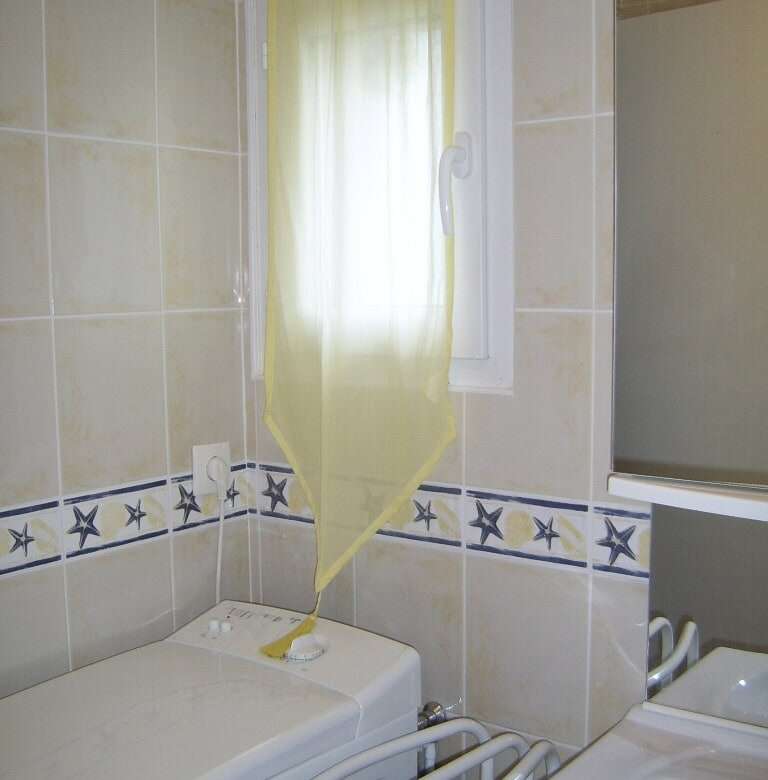Interior view of a laundry room in a seaside house with washing machine and window.