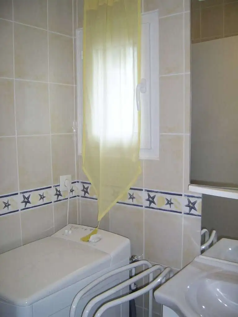 Interior view of a laundry room in a seaside house with washing machine and window.