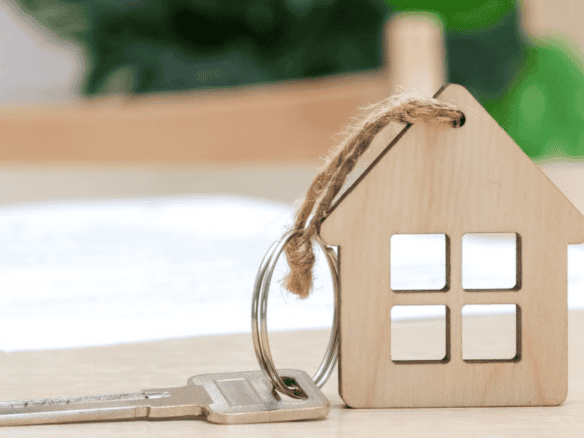 Key and wooden house model representing property ownership and real estate investment.