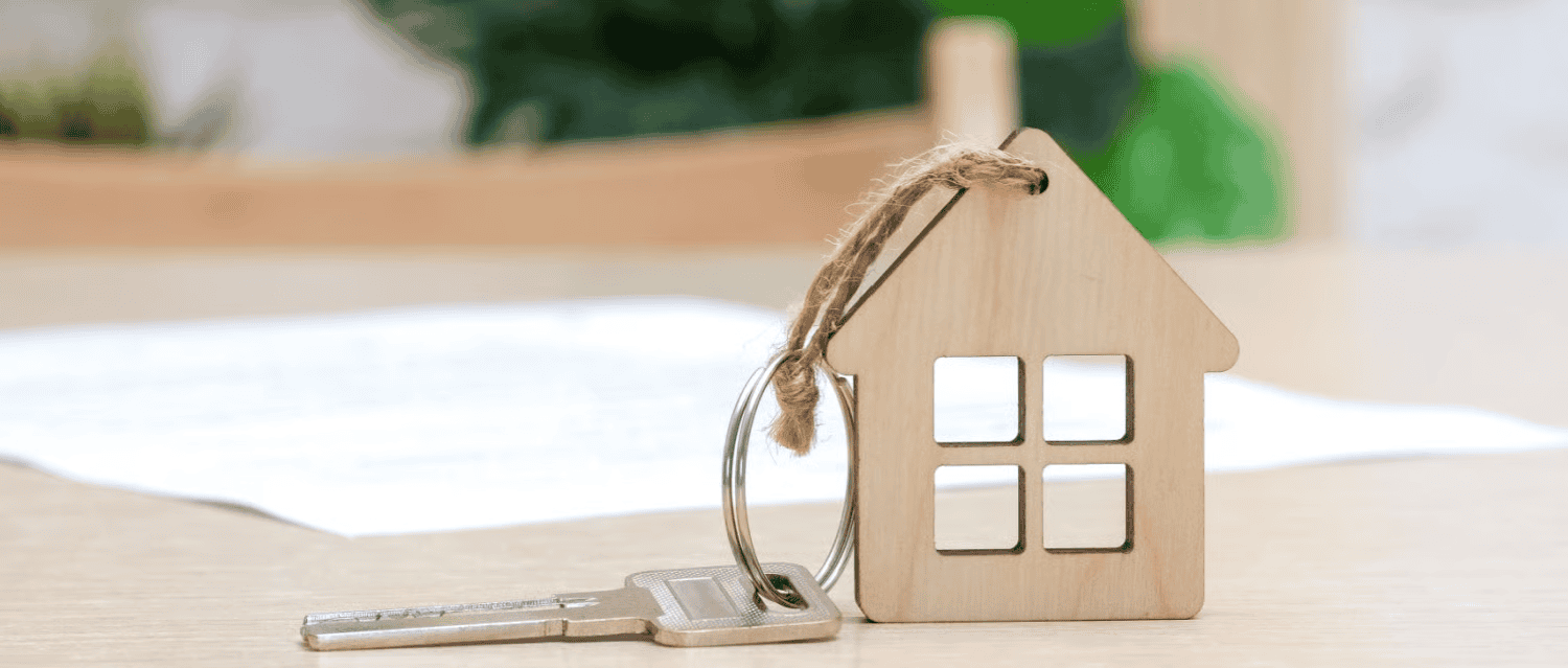 Key and wooden house model representing property ownership and real estate investment.