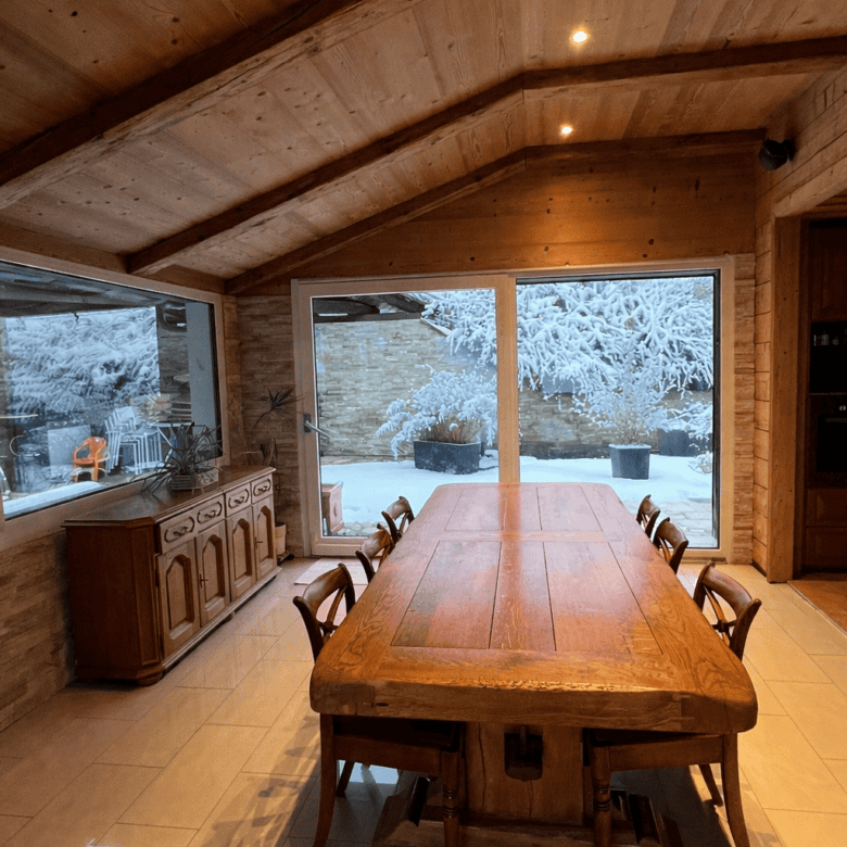 Cozy Swiss chalet interior featuring a wooden dining table and large windows overlooking snowy mount.
