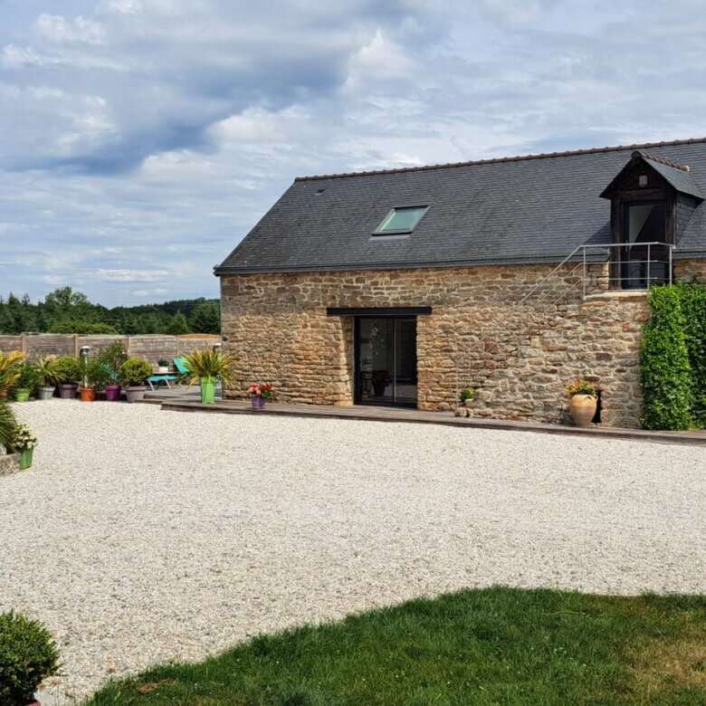 Beautiful estate in Brittany with a spacious gravel courtyard, lush plants, and traditional stone bu.