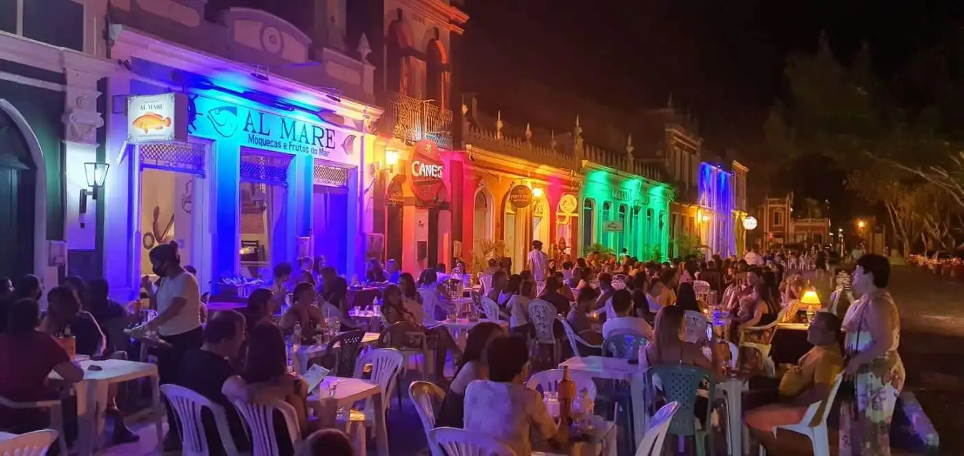 Vibrant illuminated restaurant exterior with outdoor dining and many guests enjoying the evening.