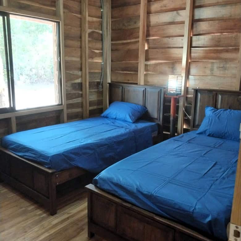 Rustic wooden bedroom with two twin beds and natural light in Vainilla, Costa Rica.