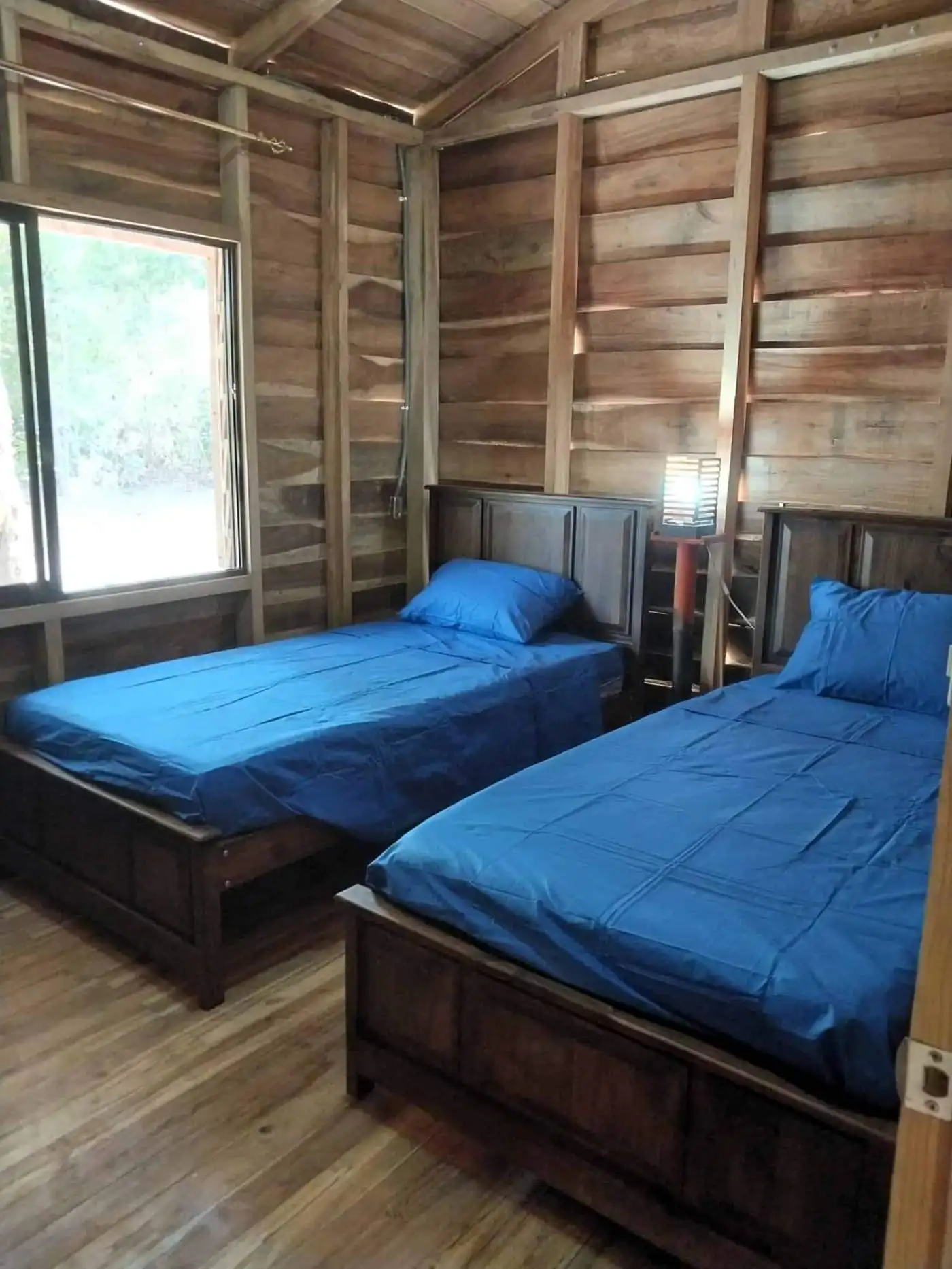 Rustic wooden bedroom with two twin beds and natural light in Vainilla, Costa Rica.