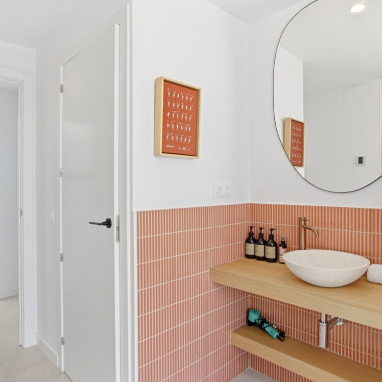 Bright and stylish bathroom featuring a round mirror and coral-colored tiles. Perfect for contempora.