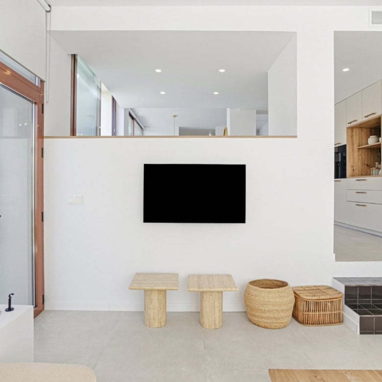 Wall-mounted TV in a bright, modern living room with minimalist furniture and natural accents.