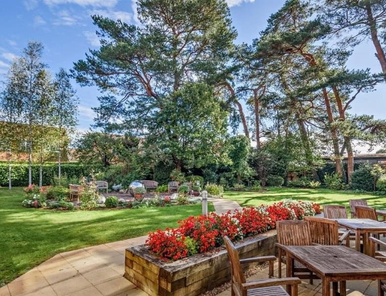 Outdoor garden with seating area, vibrant flowers, and tall trees in Hampshire, UK.