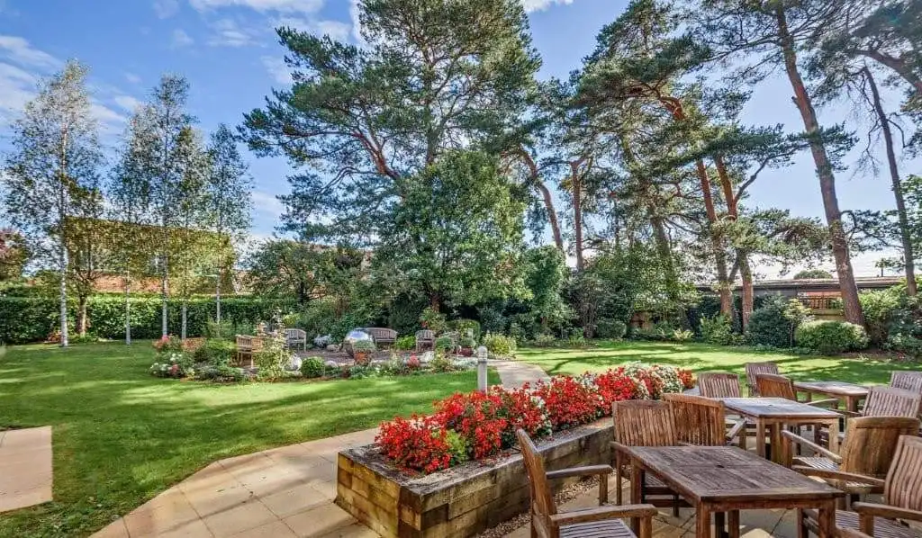 Outdoor garden with seating area, vibrant flowers, and tall trees in Hampshire, UK.
