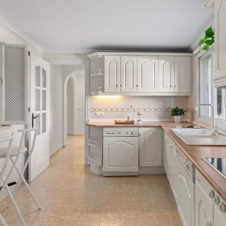 White kitchen with sea view and natural light, featuring cabinetry, countertops, and appliances.