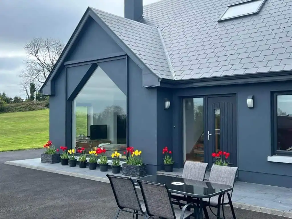 Contemporary blue house with large glass windows and colorful potted plants outside.