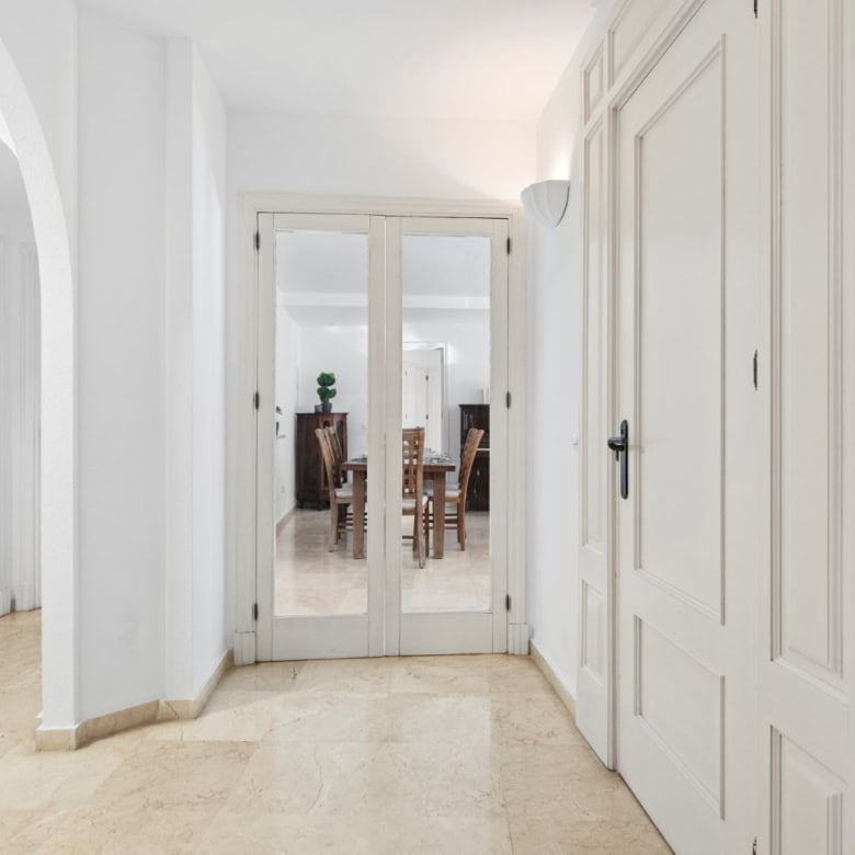 Elegant interior entrance with white walls and double glass doors leading to a spacious living area.
