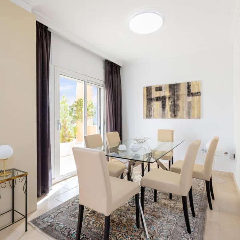 Refurbished townhouse dining area with glass table and elegant beige chairs.