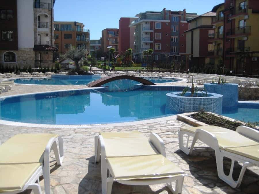 Pool area with sun loungers and garden views in Ravda apartments.