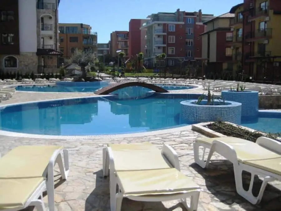 Pool area with sun loungers and garden views in Ravda apartments.