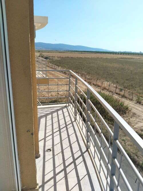 Balcony of a modern furnished apartment overlooking open fields and distant mountains, perfect for r.