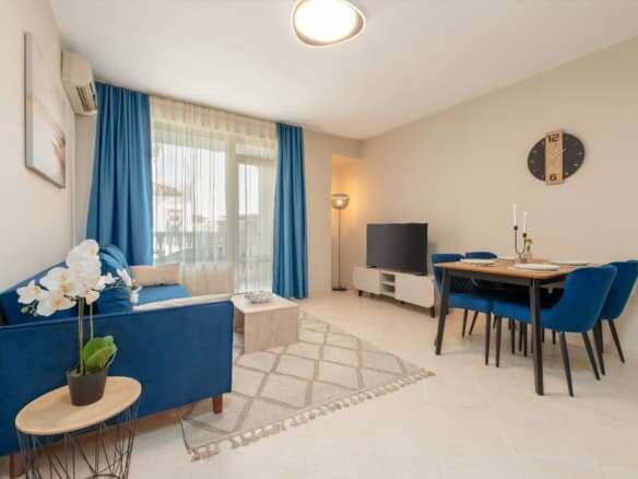 Bright living room with blue sofa, dining area, and pool view in Sunny Beach apartment.