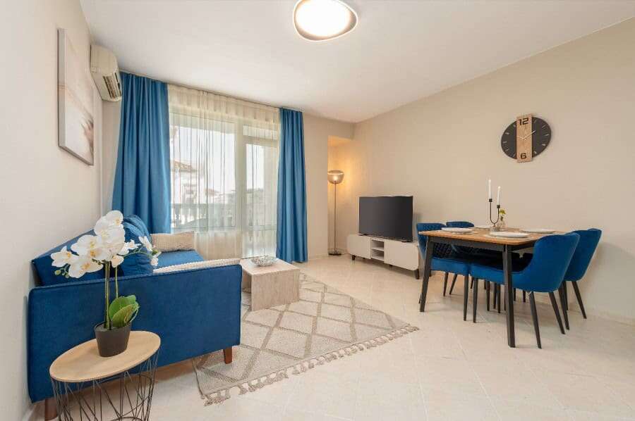 Bright living room with blue sofa, dining area, and pool view in Sunny Beach apartment.