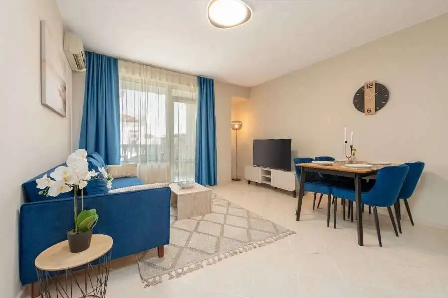 Bright living room with blue sofa, dining area, and pool view in Sunny Beach apartment.