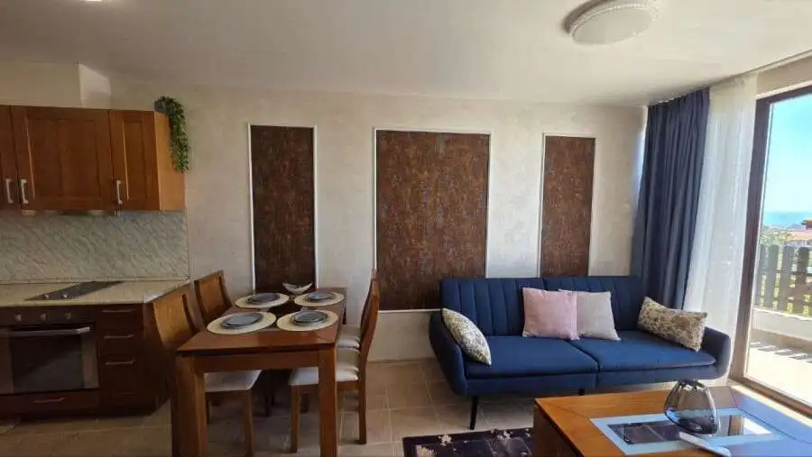 Bright living space featuring a blue sofa, dining area, and balcony overlooking scenic surroundings.