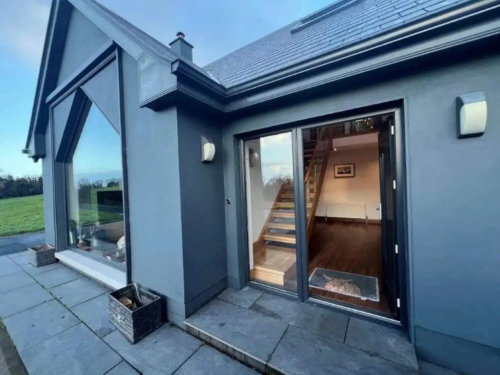 Modern gray house exterior with sliding glass door and outdoor patio.