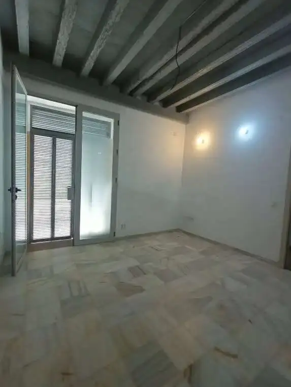 Spacious room with large glass door, marble flooring, and exposed ceiling beams.
