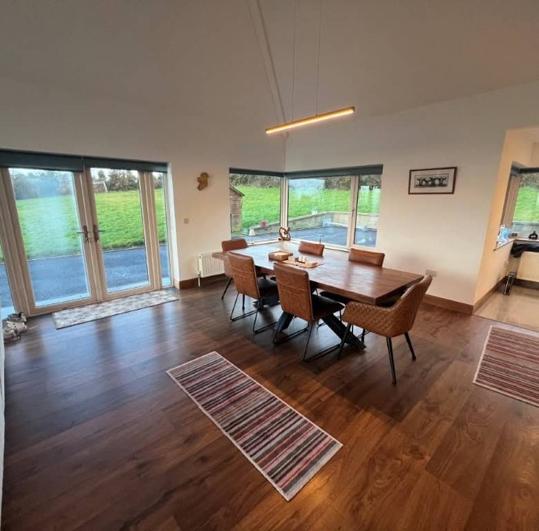 Spacious dining area featuring large windows with scenic countryside views. Modern decor and hardwoo.