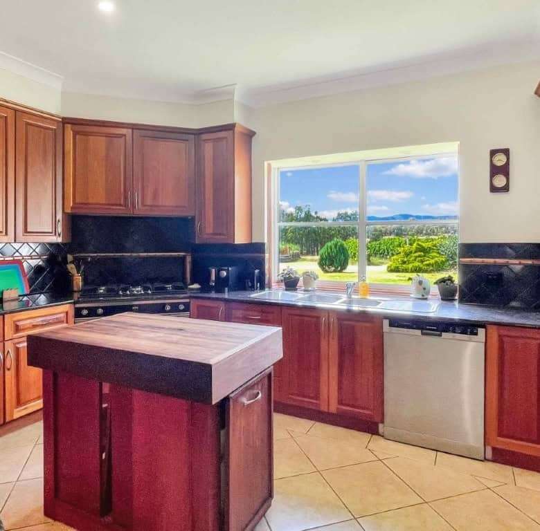 Spacious kitchen featuring wooden cabinets and a large window overlooking vineyards and rolling hill.