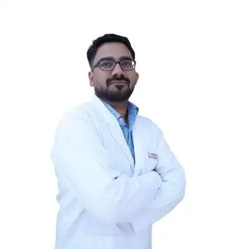 Doctor in white coat with glasses, standing confidently with arms crossed.