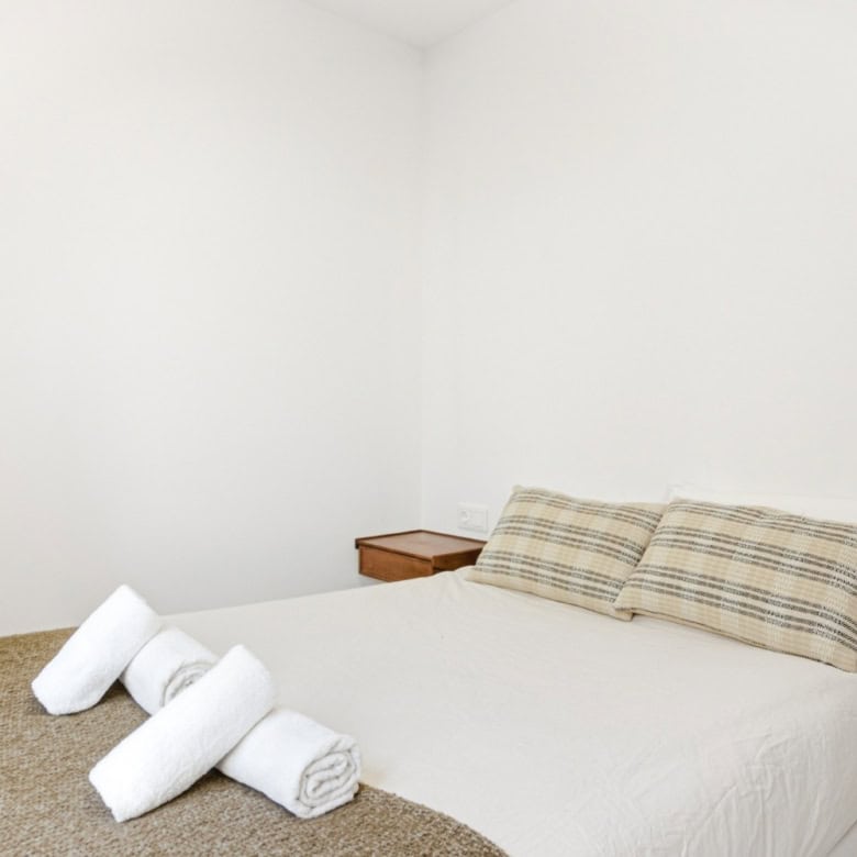 Bright bedroom with neatly made bed and rolled towels, showcasing modern interior design.