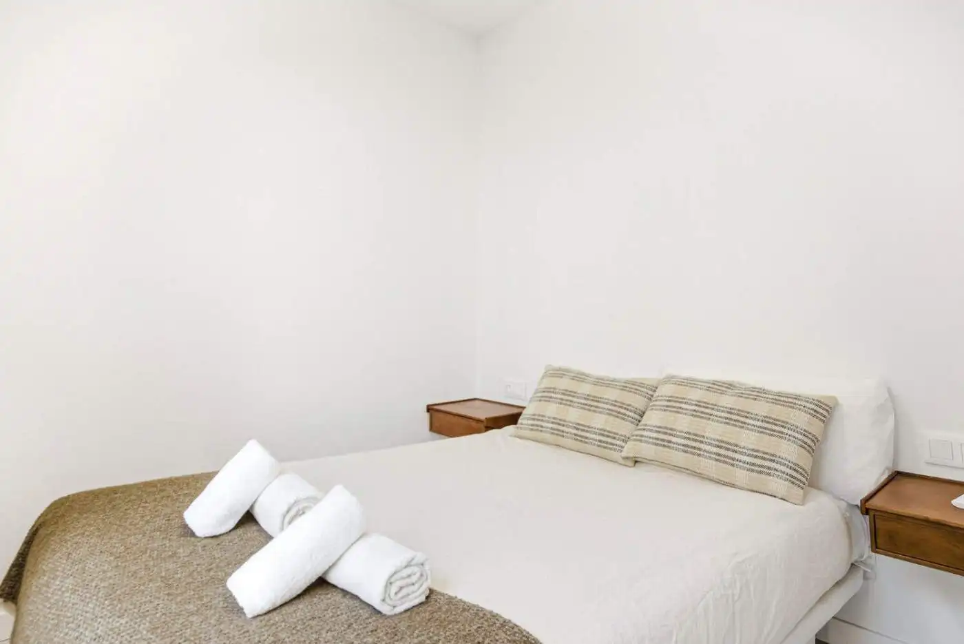 Bright bedroom with neatly made bed and rolled towels, showcasing modern interior design.