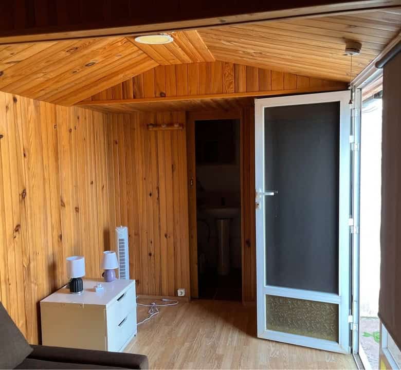 Mobile home interior with wooden walls and ceiling, featuring a door leading to an outdoor space.