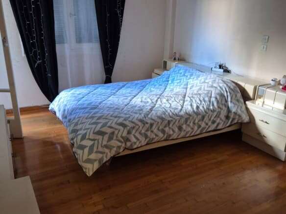 Bright bedroom with large window and black curtains in Athens apartment.