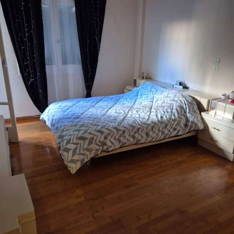 Bright bedroom with large window and black curtains in Athens apartment.
