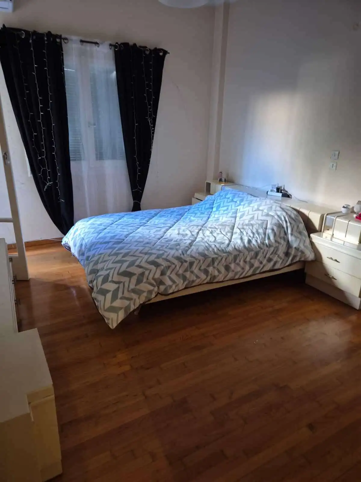 Bright bedroom with large window and black curtains in Athens apartment.