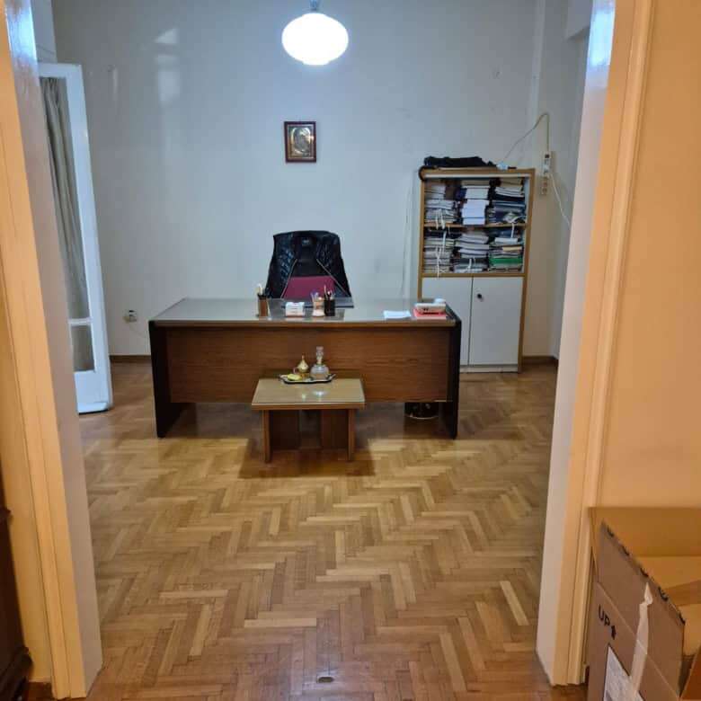 Office space with wooden desk, black chair, and bookshelf in a bright room.