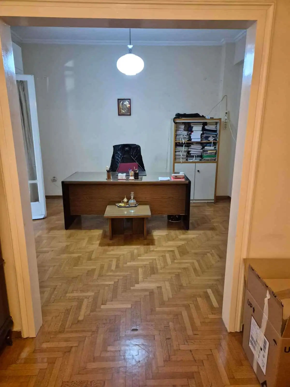 Office space with wooden desk, black chair, and bookshelf in a bright room.